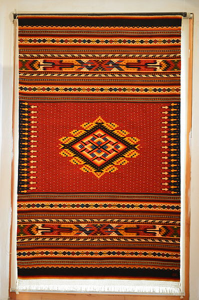 Woven rug in traditional design at the exhibition La Mano Mágica by Arnulfo Mendoza at the Museo de los Pintores Oaxaqueños in the city of Oaxaca, Mexico. Attribution: AlejandroLinaresGarcia